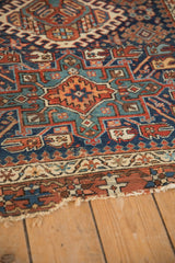Worn, tattered corner and geometric navy blue, rust, and ivory borders of the Karaja rug.