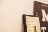 Antique eye plaque's dark wood frame, brass rivet, and small near vision text.