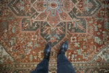 Distressed vintage Heriz rug, rust field, intricate geometric patterns, and soft blue accents.
