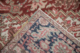 Distressed Heriz carpet folded corner, showing geometric red, beige, navy pattern, surface wear, and foundation weave.
