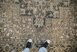 Vintage distressed Heriz rug, geometric patterns in beige, charcoal, and dusty teal with visible wear.