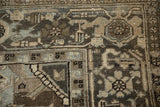 Distressed vintage Heriz carpet corner with muted beige, charcoal, and dusty teal traditional motifs.