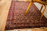 Corner of a vintage Hamadan rug, showing ivory fringe and red, time-softened Herati pattern.