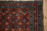 Corner of vintage Mehriban rug with burgundy field, geometric borders, and tattered fringe.