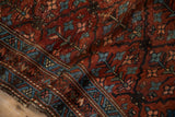 Close-up of vintage Persian Mehriban rug with sapphire blue geometric border and worn burgundy field.