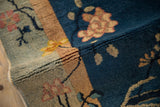 Rug's folded pile showing cobalt blue, seafoam green, and golden lotus flowers and branches.