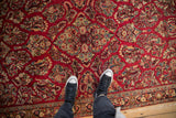Detailed view of the dense floral bouquets covering the cherry red field of a vintage Sarouk rug.