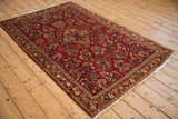 Vintage Sarouk rug with intricate florals on a cherry red field, shown from an angled perspective.