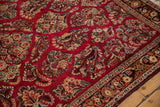 Corner view of a vintage Sarouk rug with intricate floral bouquets on a cherry red field.