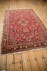 A traditional vintage Sarouk rug with a cherry red floral field, shown from a three-quarter perspective.