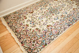 Vintage Kerman rug with intricate floral border in ivory, light blue, and pink, showing fringe.