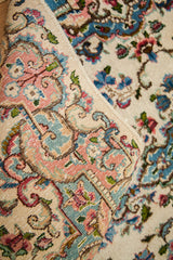 Curled edge of an Ivory Kerman rug, showing pink, blue, green European floral border.