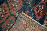 Visible hand-knotted foundation, fringed edge, and red, navy geometric motifs on an antique Caucasian rug.