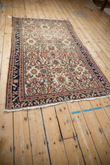 Antique Malayer rug shown at an angle, detailing its ivory field and serrated vine navy border.