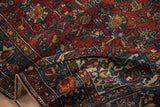 Folded antique Malayer rug showing the texture of its intricate, gem-toned floral and vine pattern.