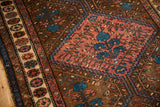Close-up view of a vintage Kurdish rug's pomegranate border and brick-red tree of life medallion.