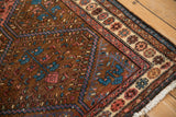 Angled view showing the worn side and pomegranate border of a vintage hand-knotted Kurdish rug.