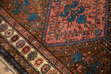 Close-up on the pomegranate border and worn wool pile of a vintage Kurdish Hamadan rug.