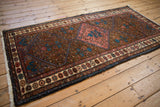 Angled view of a vintage Kurdish Hamadan rug with a rose medallion and pomegranate motif border.