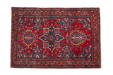 Vintage Persian Karaja rug with a staggered blue quatrefoil medallion on a vibrant cherry red background.
