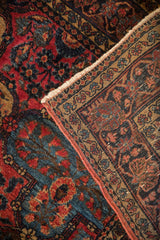 Antique Sarouk rug: red and navy floral pile, worn knot heads, and woven selvage detail.