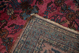Folded corner of vintage Lilihan rug showing magenta floral pile and intricate vine border.