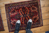 A small vintage Sarouk rug with a red and navy floral pattern, viewed from overhead to show scale.
