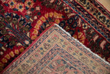 The hand-knotted back and rich cherry red pile of a vintage Sarouk rug corner.
