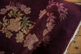 A rolled antique Art Deco rug showing its varied pile height and floral details on an aubergine field.
