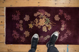 A person's view looking down at an antique Art Deco rug with a rich aubergine and gold floral pattern.