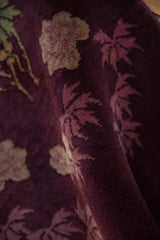 Angled view highlighting the textured pile and floral bouquets on an aubergine Art Deco rug.