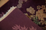 Corner of an antique floral rug folded to show the hand-knotted aubergine foundation.