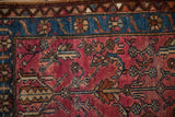 Close view of the hand-knotted texture on the raspberry red field and sapphire blue floral border.