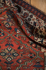 Tactile view of a folded vintage Malayer rug highlighting the plush brick red pile and indigo border.