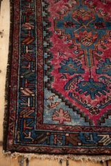 Detail of a vintage rug's varied color density in its raspberry red field and blue geometric border.