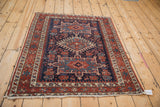 Fringed corner of antique Karaja rug, revealing worn pile, madder red, and dark blue geometric designs.