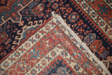 Folded antique Karaja rug, featuring dark blue geometric field, brick red border, ivory fringe.