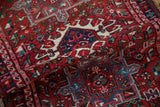 Textured fold of vintage Karaja rug, highlighting geometric blossoms in cherry red and sky blue.