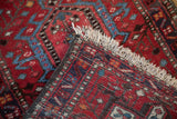 The folded corner of a vintage Karaja rug runner reveals its hand-knotted foundation and brick-red pile.
