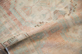 A gentle fold in the distressed vintage Oushak rug reveals its soft, low pile and hand-knotted texture.