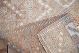 Distressed vintage Melas rug pile in coffee, copper, and ivory with visible side selvage.