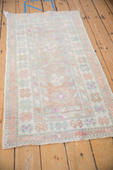 Angled view of a distressed Oushak rug with a faded floral pattern in dusty rose and seafoam green.