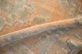 Distressed Oushak rug, rolled to show soft pile and faded sandalwood, mint, and slate blue.