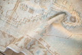 Distressed Oushak rug pile showing geometric patterns in faded beige, bronze, and pale blue.