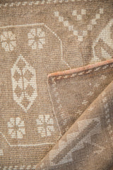 Distressed Melas rug: close-up of worn pile, ivory geometric motifs, and original side cording.