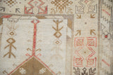 Distressed pile of vintage Melas rug, featuring ivory, dusty bronze, and red stepped patterns.
