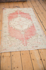 Angled view of a distressed Oushak rug showing its faded cherry red medallion and time-softened texture.