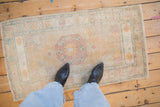 A distressed vintage Oushak rug runner showing its scale and faded medallion in dusty gold and mauve.