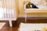 A modern white maple bench functioning as a sidecar next to a crib.