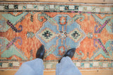 Overhead of vintage Oushak runner: faded blue shield medallion, rust abrashed field, turquoise vines.
